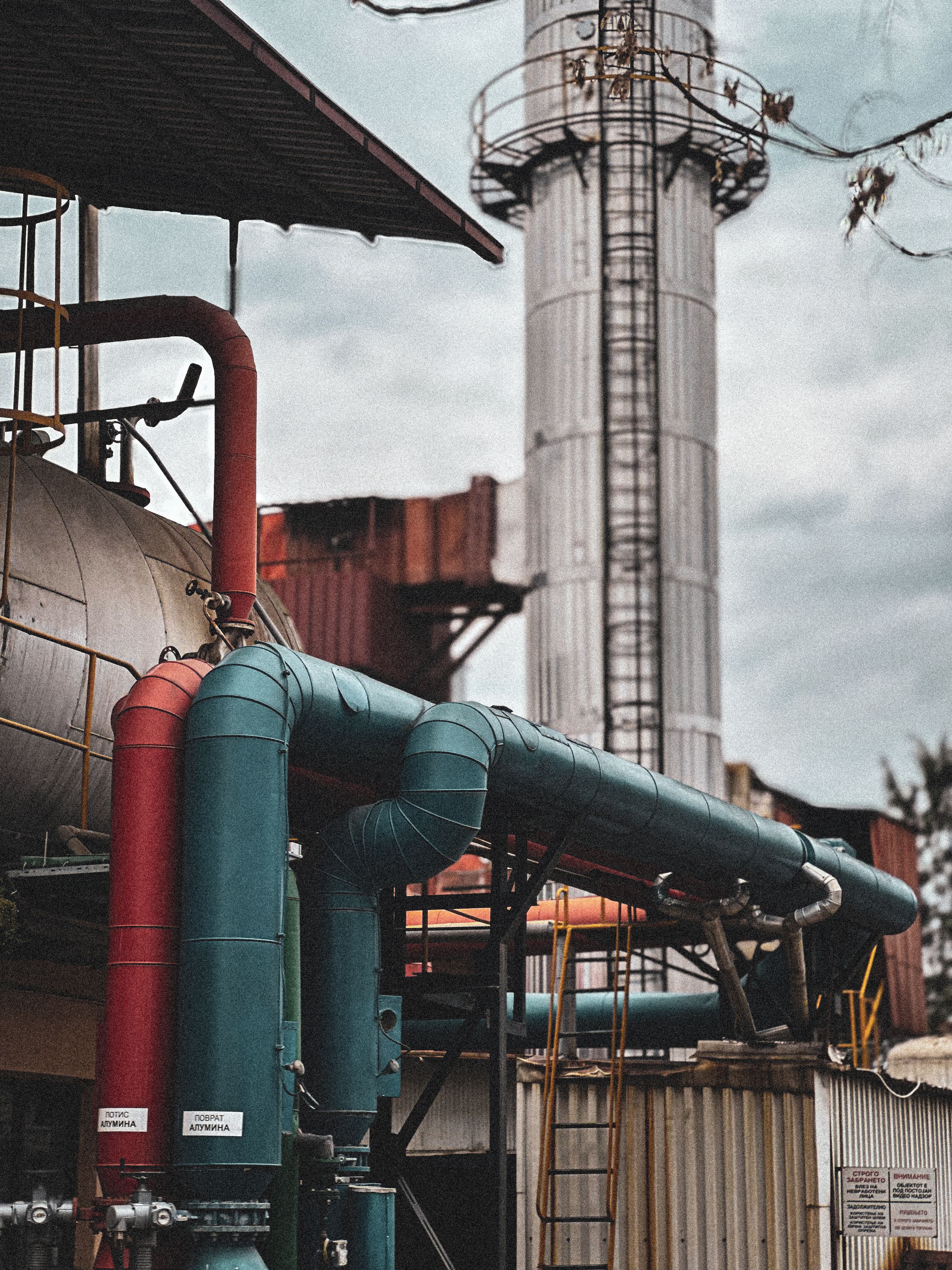 Photo by worldofmtc on Pexels Industrial storage tank with red and teal pipework beside a tall processing tower