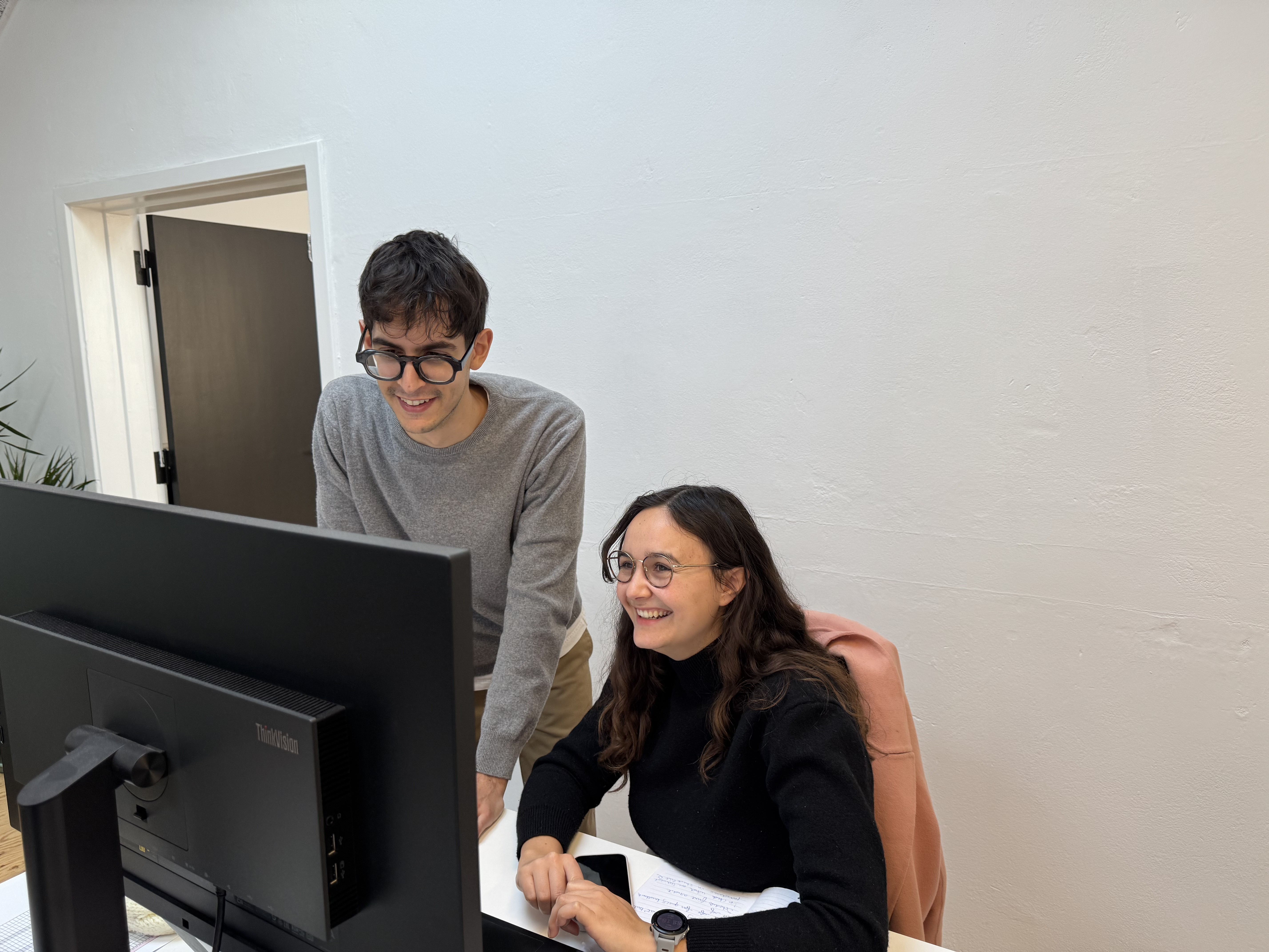 Two colleagues laughing together at a desktop computer in the office