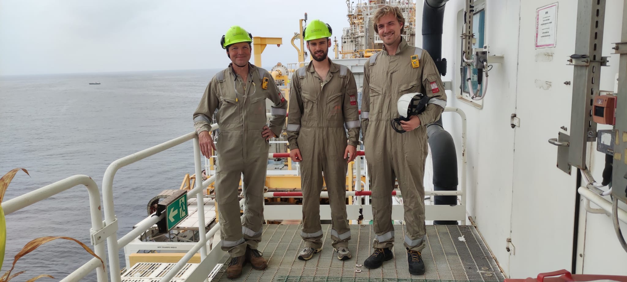 Three colleagues in safety gear and hard hats on an offshore platform